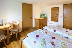 Een kamer met twee bedden, een houten bureau, een stoel, een televisie op een kast en een deur.