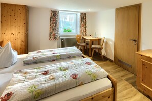 Een slaapkamer met twee bedden, een houten bureau, een stoel, een radiator en een raam met gordijnen.