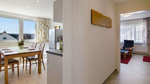 Een moderne eethoek met een houten tafel en stoelen, een keuken op de achtergrond en uitzicht door het raam.