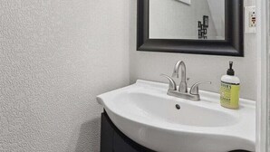 A bathroom with a white sink, dark cabinets, a black-framed mirror, and two wall-mounted light fixtures.