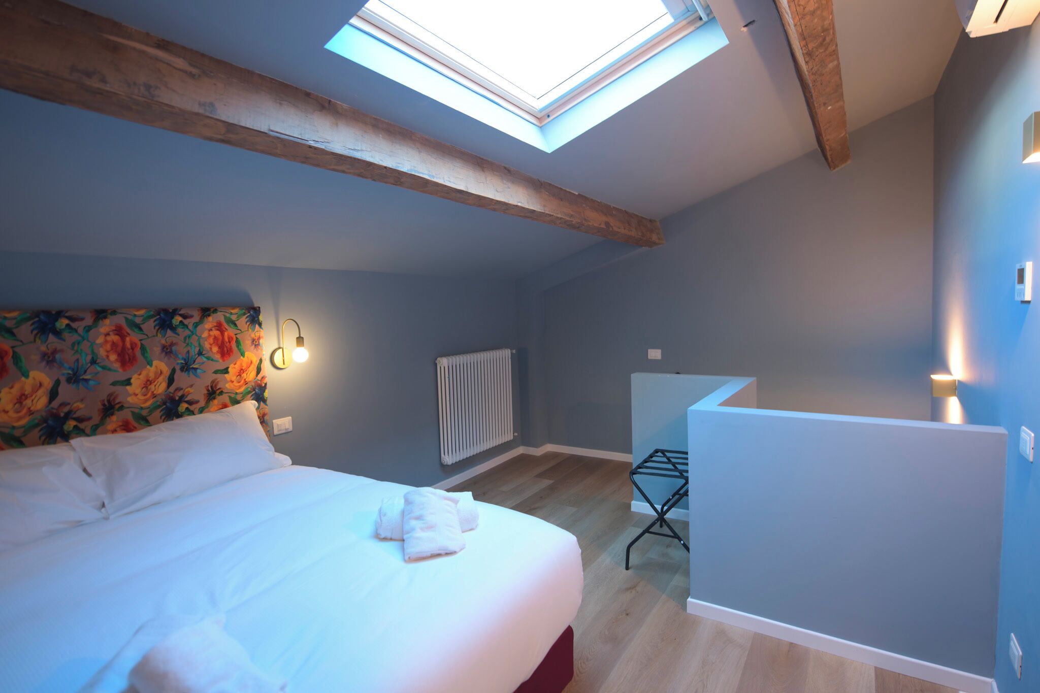 A bedroom with a bed, a skylight, a radiator, and a small desk area.