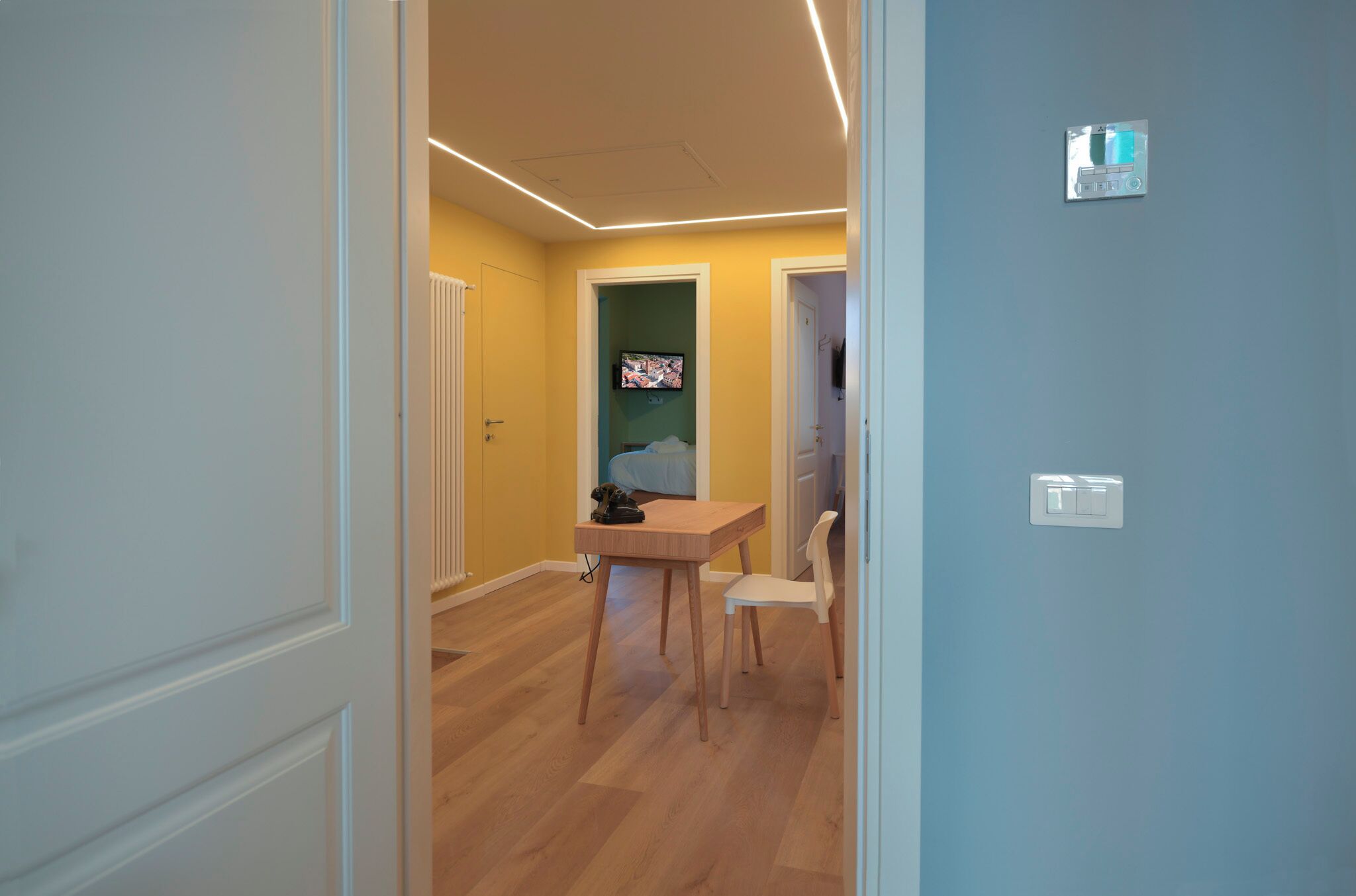 Una stanza con pavimento in legno, un tavolo con una sedia, un televisore a parete e un interruttore della luce.