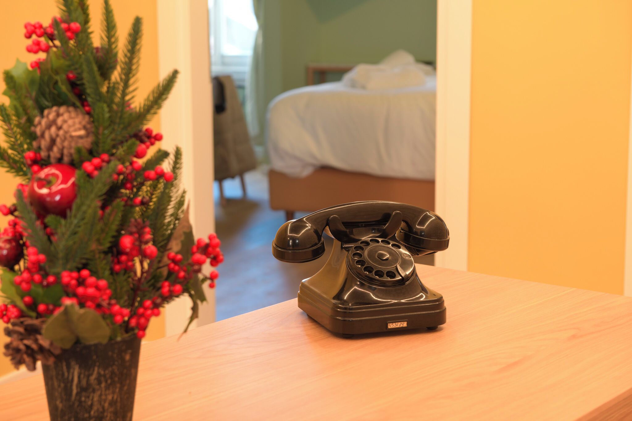 A wooden table with a vintage rotary phone and a Christmas tree with red berries and pinecones.