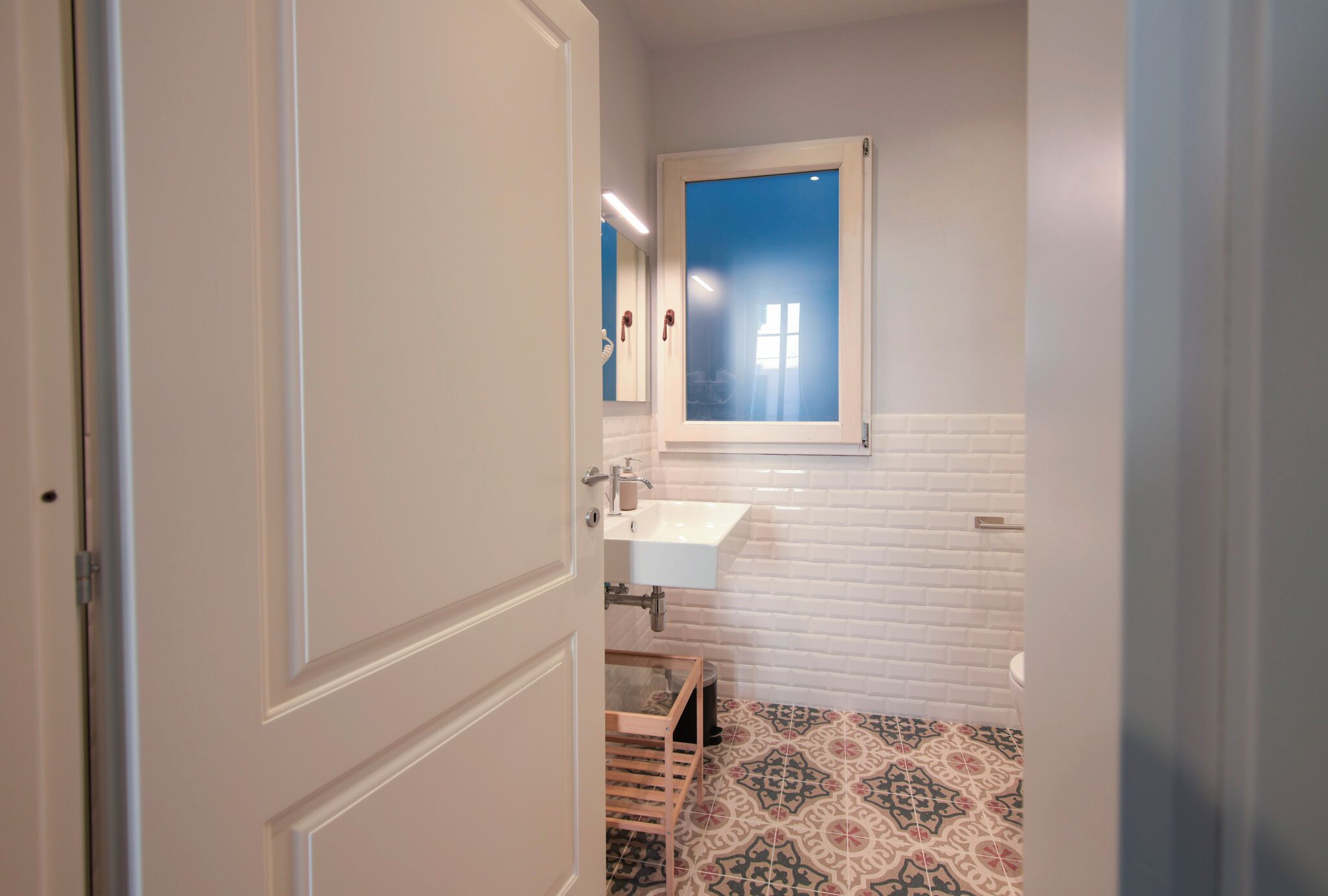 A bathroom with a white sink, a window, and patterned floor tiles.