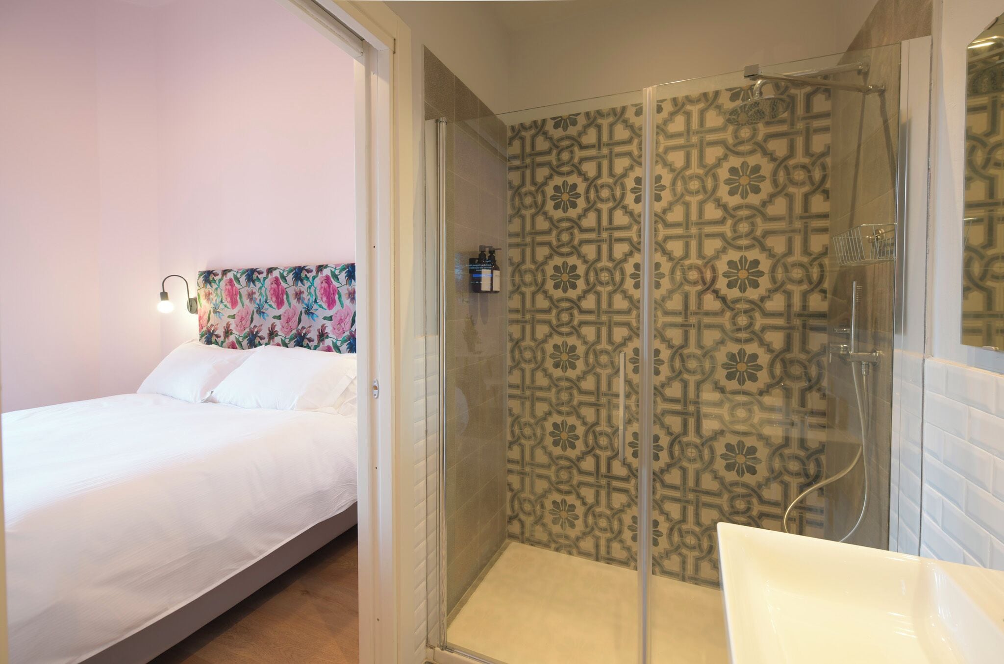 Une chambre d’hôtel avec un lit, une douche dont le mur est décoré d’un motif, et une salle de bain avec un lavabo.
