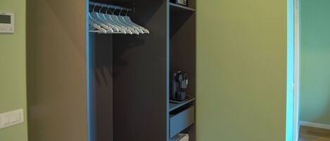 Un vestidor con ropa colgada, una cafetera y un pequeño electrodoméstico.