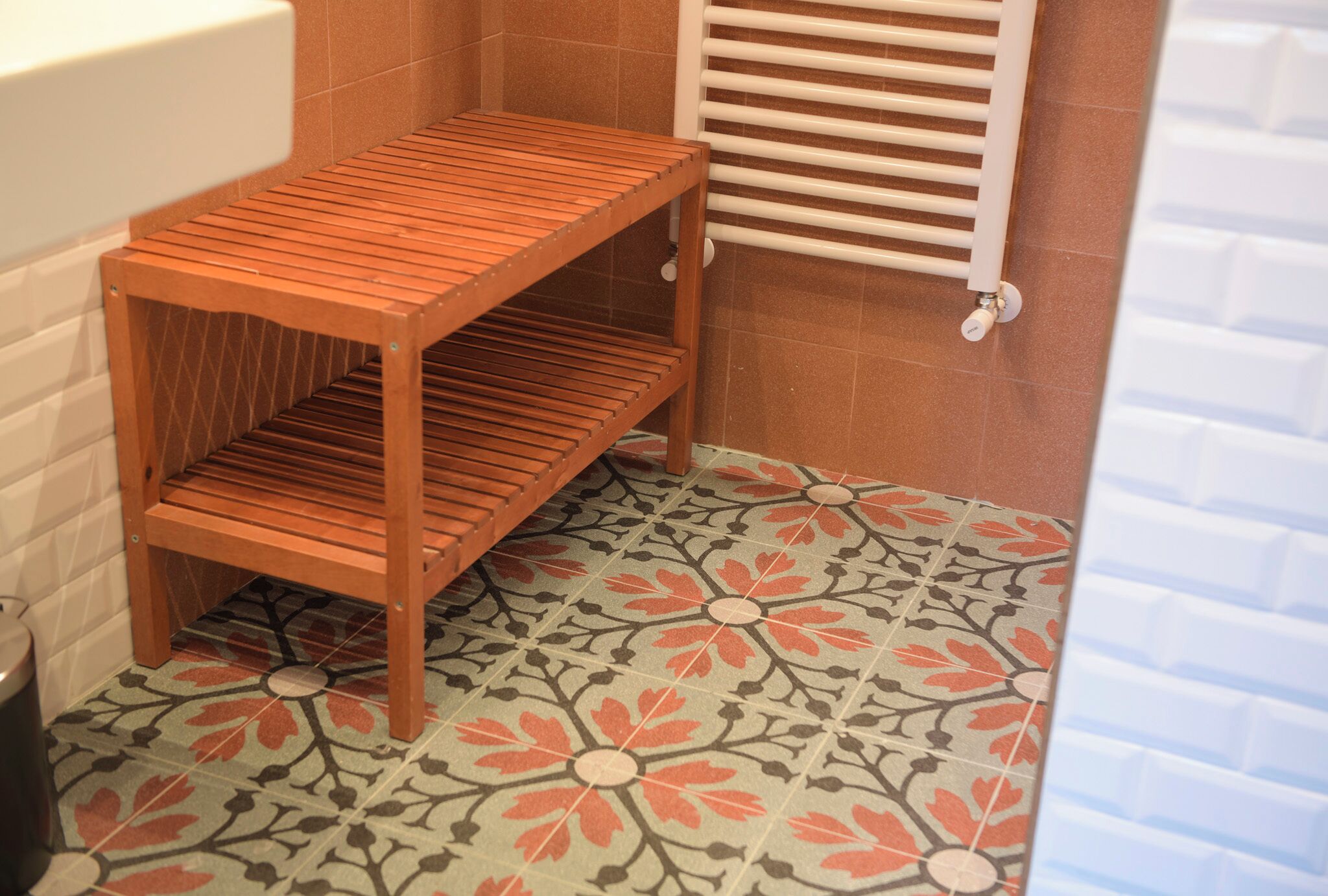 A bathroom with a wooden shelf, a white radiator, and patterned floor tiles.
