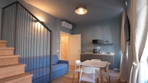 A modern apartment with a staircase, a blue sofa, a dining table with chairs, a kitchen area, and a ceiling light. - B&B Magnolia (Florence)