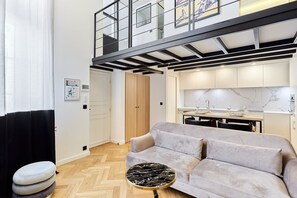 A modern living room with a sofa, a round coffee table, and a kitchen area with a marble backsplash. - Charming Duplex Loft - Paris City Center (Paris)