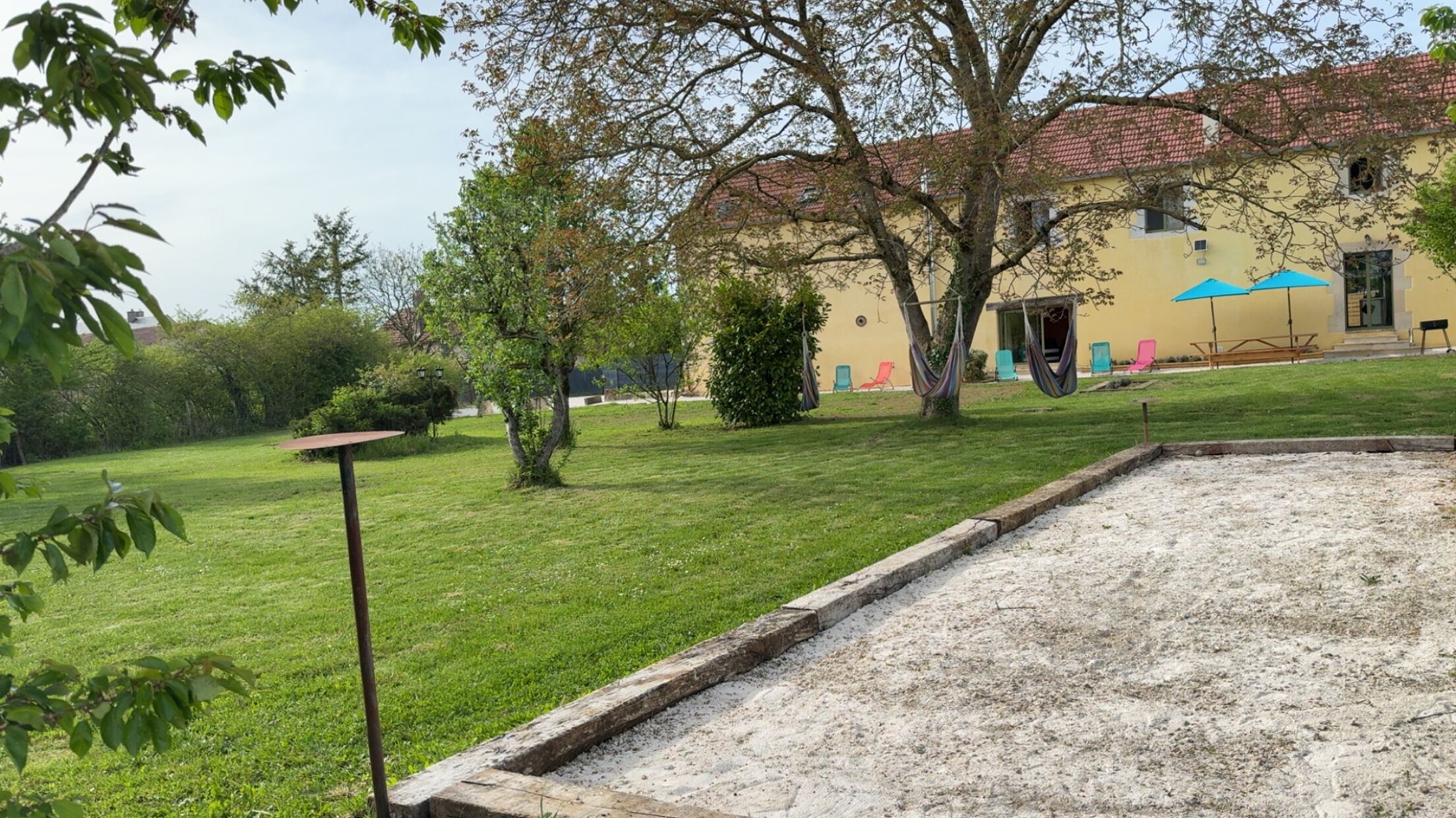 Une cour avec une pelouse verdoyante, un hamac et un bâtiment doté d’un toit en tuiles.