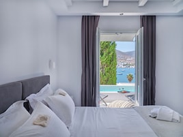 Un dormitorio con cama, almohadas y vistas a una piscina y al paisaje urbano.