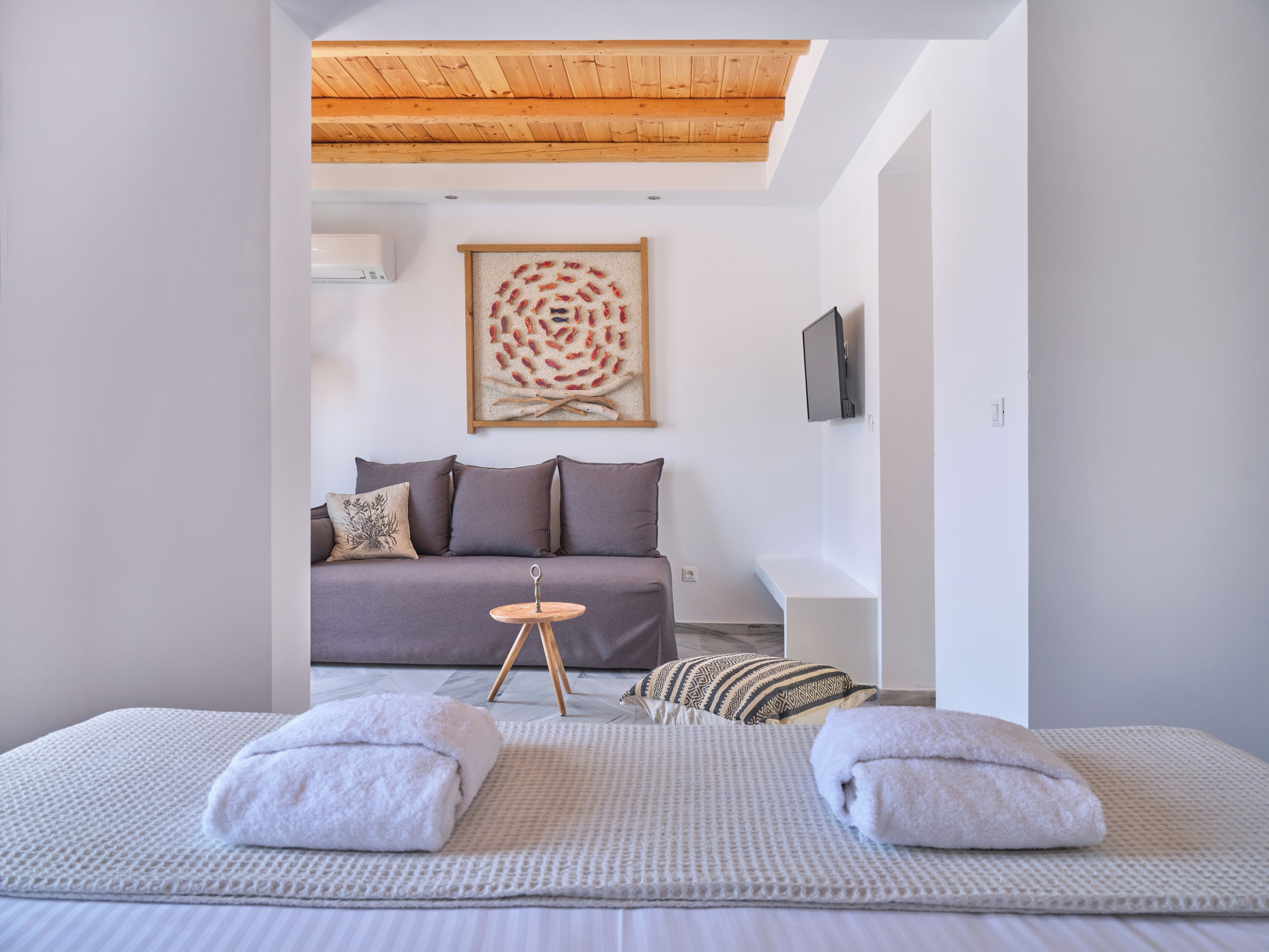 Une chambre à coucher moderne avec un lit, une petite table, un téléviseur et une œuvre d’art murale.