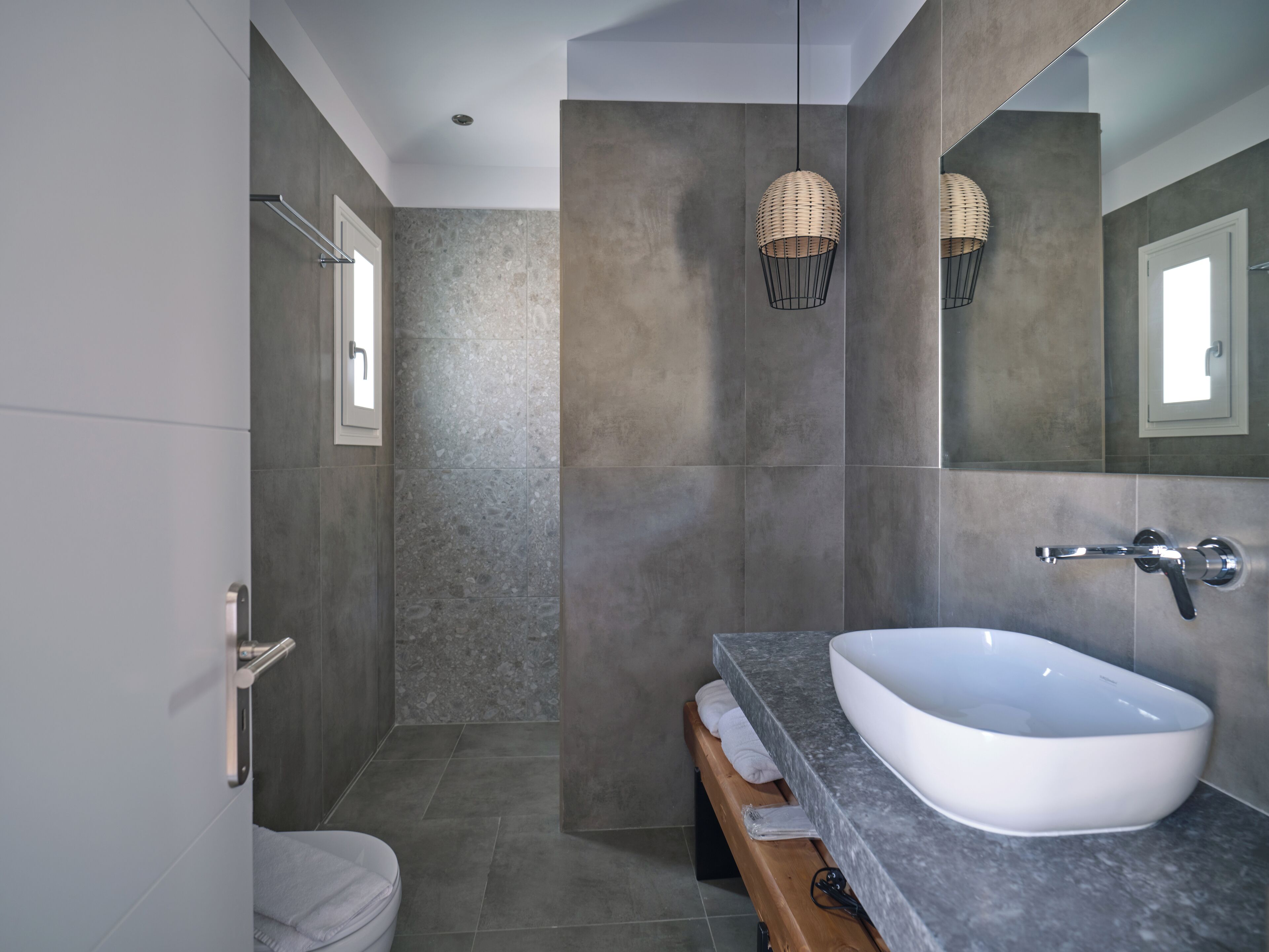 Un baño moderno con un lavamanos grande de color blanco, un banco de madera y una zona de ducha.