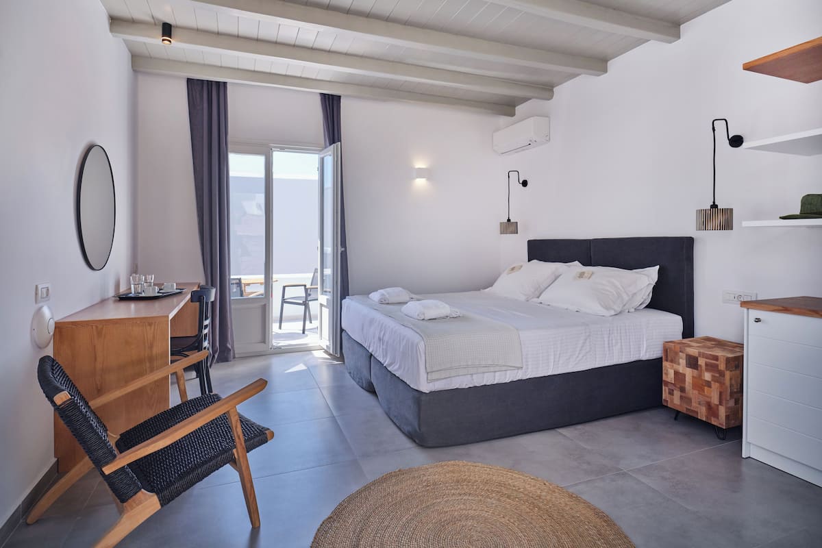 Un dormitorio moderno con una cama grande, un escritorio con silla, una mesita y un balcón con vistas.