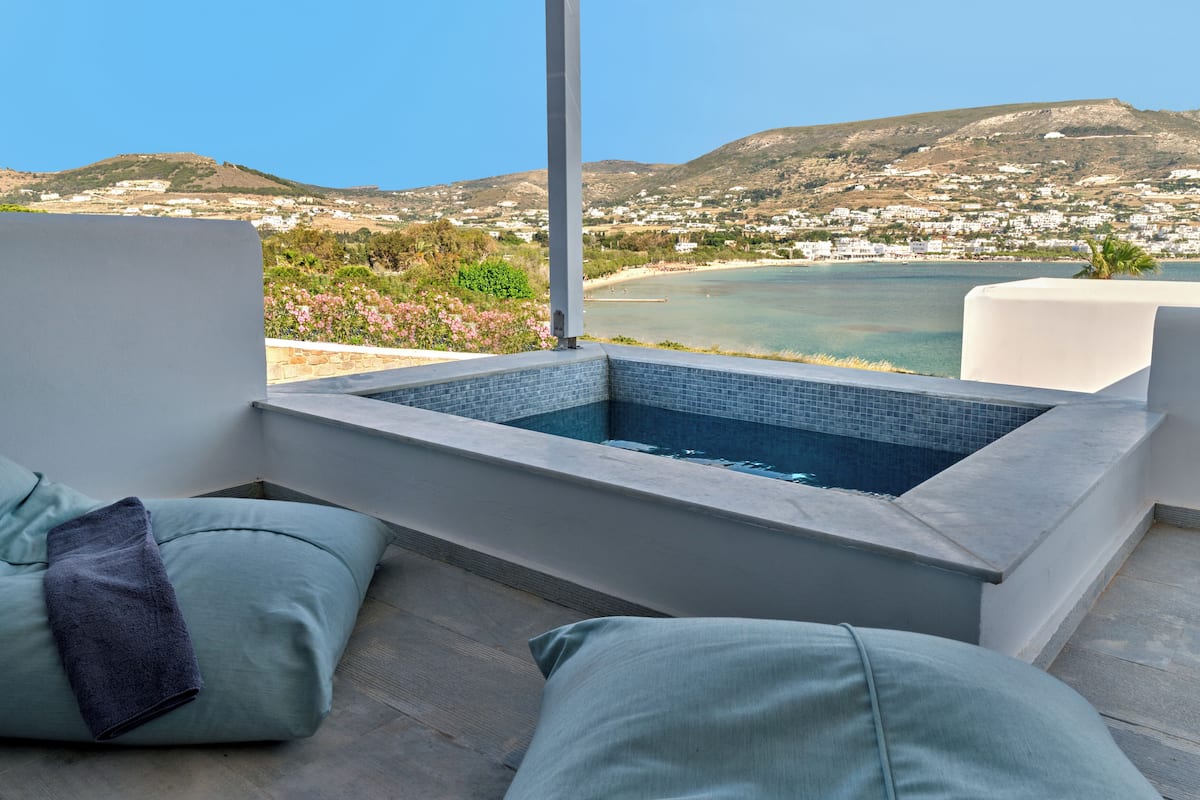 Un área de estar moderna al aire libre con un jacuzzi integrado, con vistas a un pueblo costero y una playa.