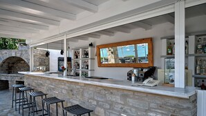 Ett utomhusområde med bar, där väggarna är klädda med sten, och som även har en stenugn och barstolar.