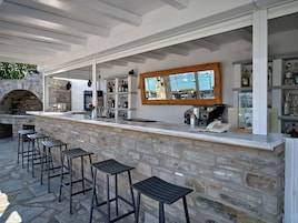 Un área de bar al aire libre con paredes de piedra, un horno de piedra y taburetes de bar.