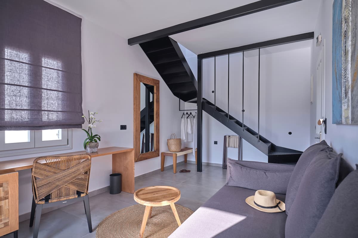 Una sala de estar moderna con un sofá, una silla de mimbre, una pequeña mesa de madera y una escalera con barandilla negra.