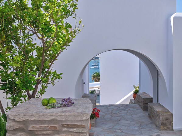 A stone pathway leading through a white archway, with a view of boats and palm trees in the background. - Parian Village Beach Hotel - Adults Only (Paros)