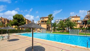 A swimming pool with a thatched umbrella, surrounded by palm trees and apartment buildings. - Perseo - Apartment In Torrevieja. Free Wifi (, Alicante)