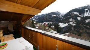 A wooden balcony with a view of snow-capped mountains and a village below. - Apartment in Zillertal near Ski Slopes (Zell am Ziller)