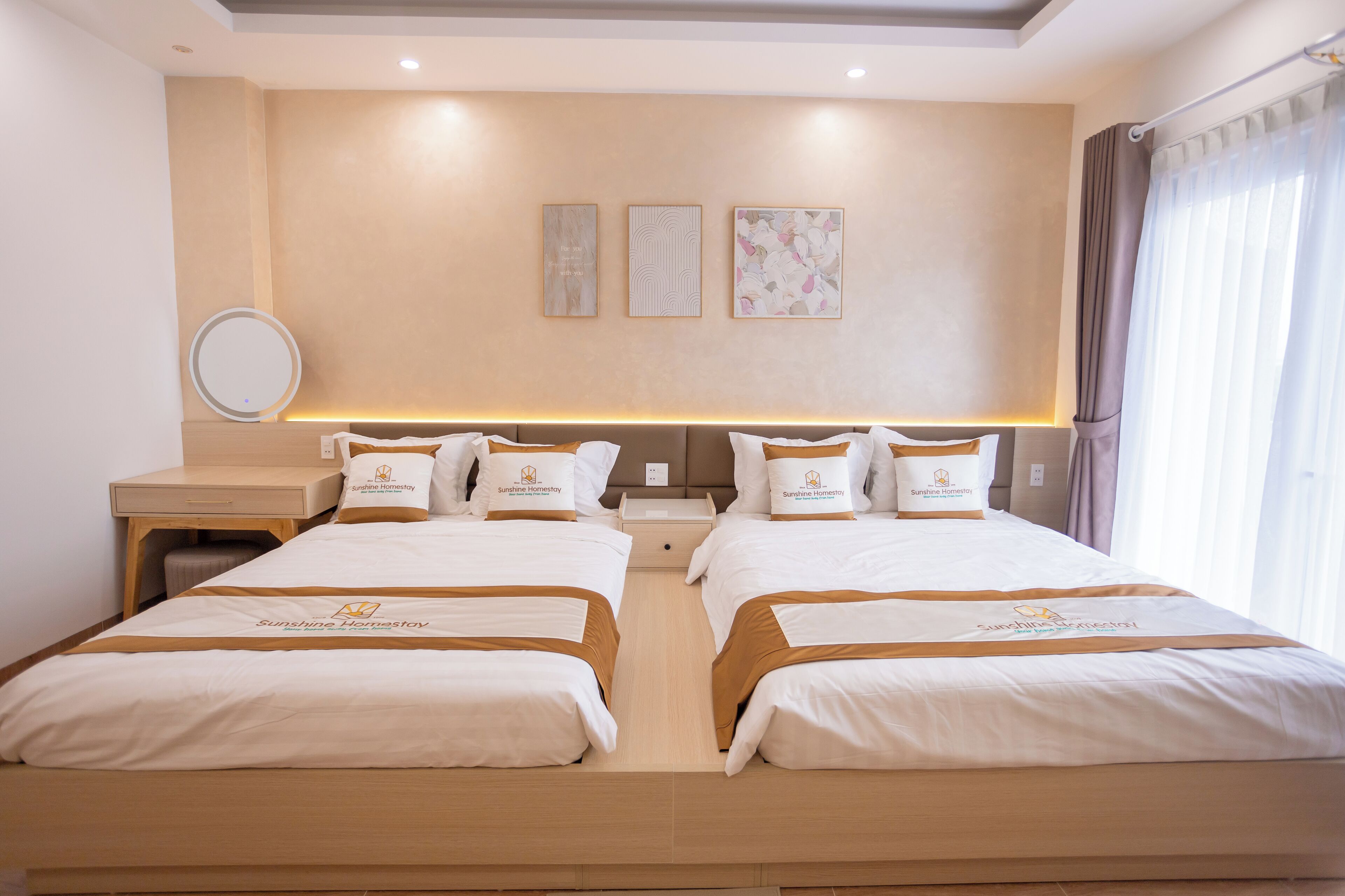 A hotel room with two beds, a bedside table, a mirror, and a wall with three framed pictures.