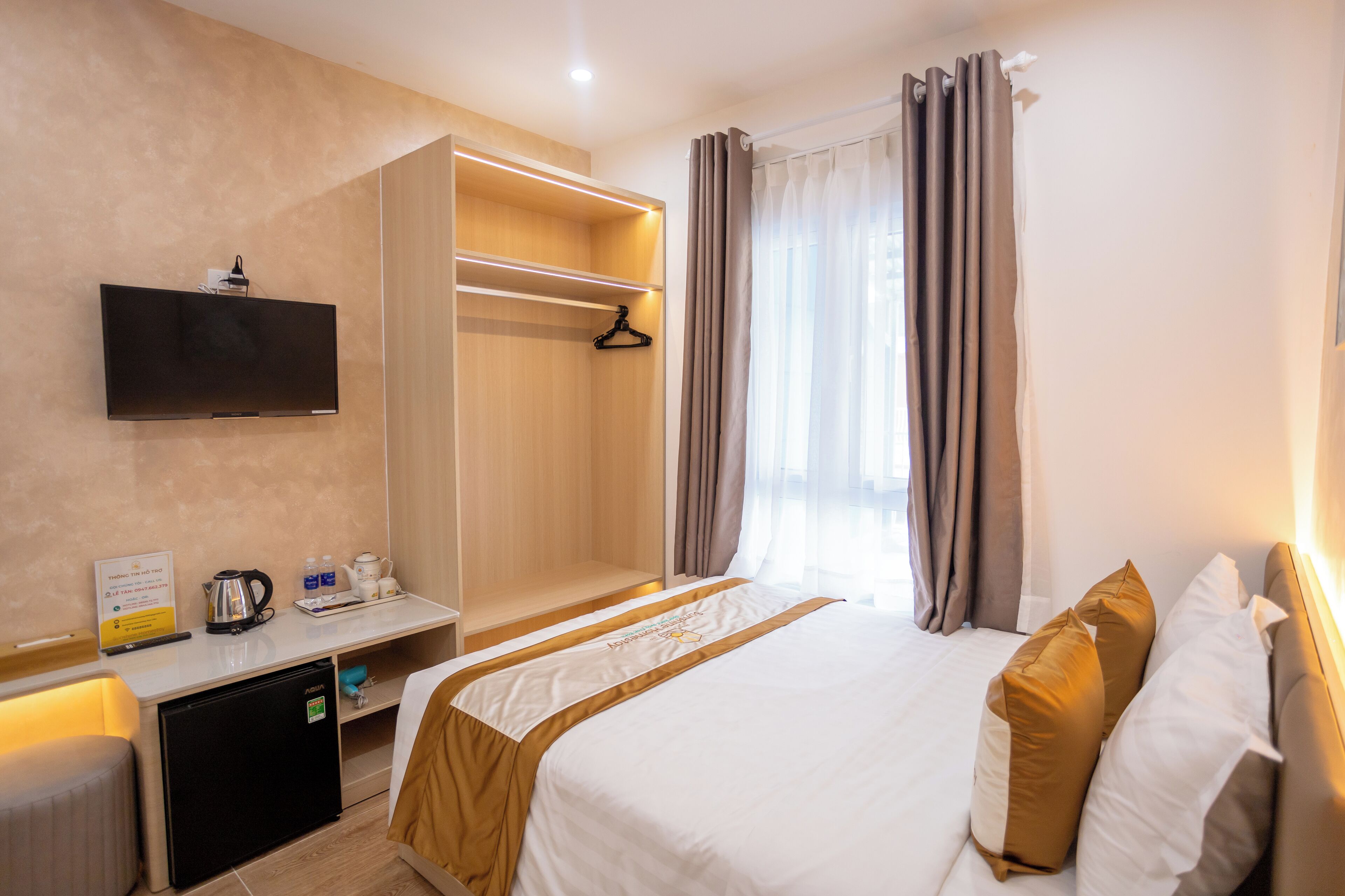 Habitació d'hotel amb llit, televisió penjada a la paret, mini-nevera, escriptori amb tetera i tasses, i armari.