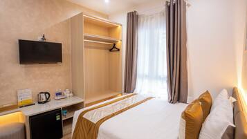 Habitació d'hotel amb llit, televisió penjada a la paret, mini-nevera, escriptori amb tetera i tasses, i armari.