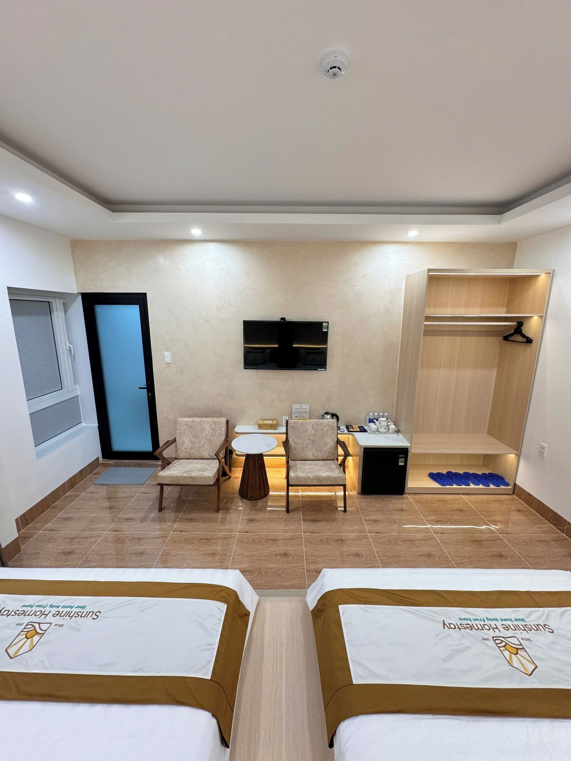 A hotel room with two beds, a desk with chairs, a TV, a coat rack, and a shoe rack.