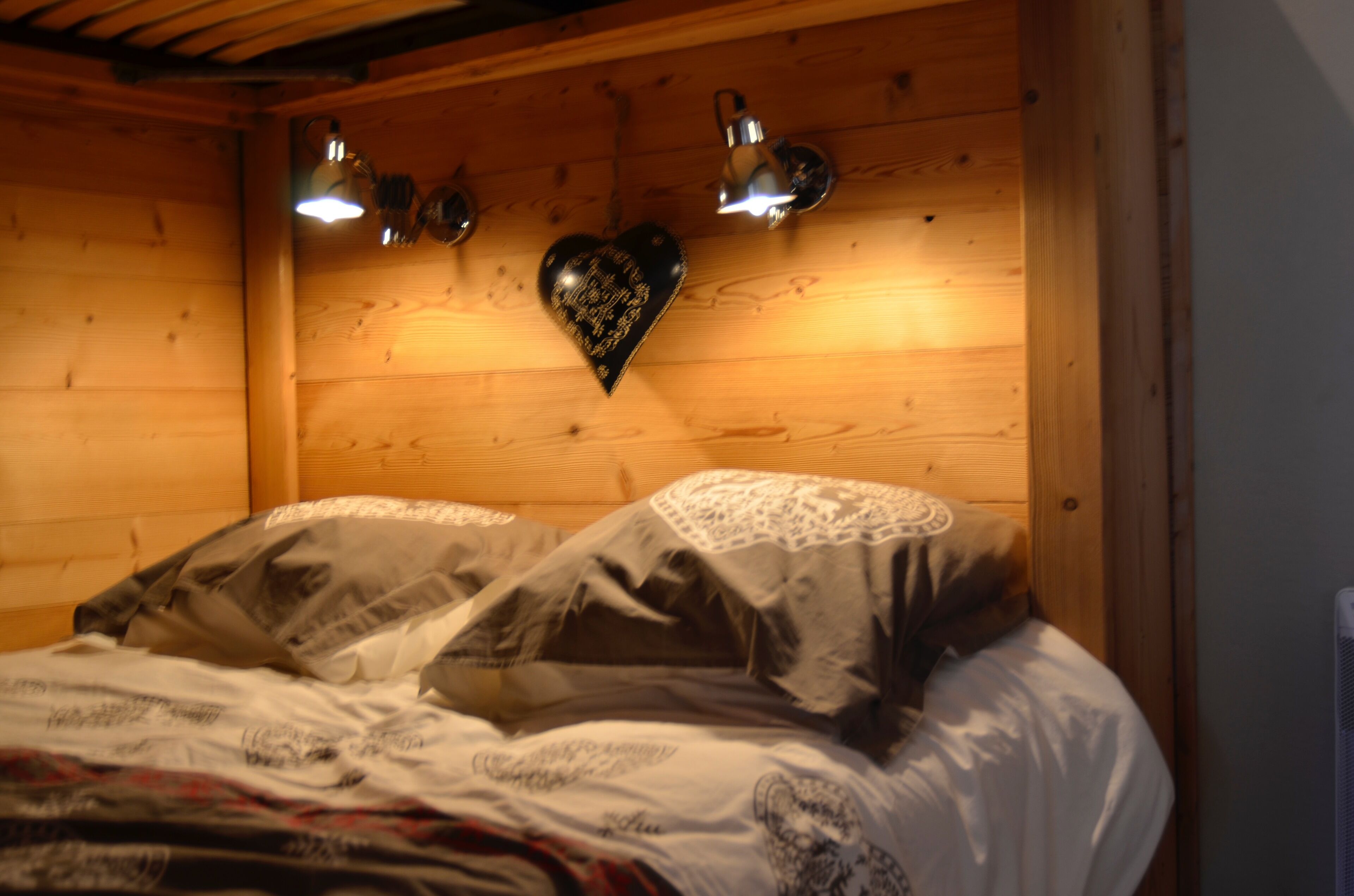 Una habitación tipo cabaña de madera con una cama, dos lámparas fijadas a la pared y una decoración con forma de corazón en la pared.