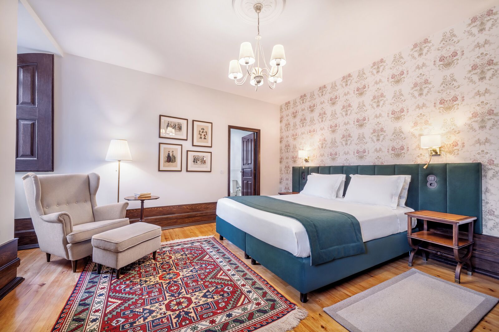 A hotel room with a large bed, a chair, a small table, a floor lamp, and a patterned rug.