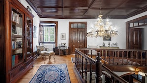 A grand room with a wooden staircase, a chandelier, and a large bookcase. - Solar das Tilias - Historic House (Seia)