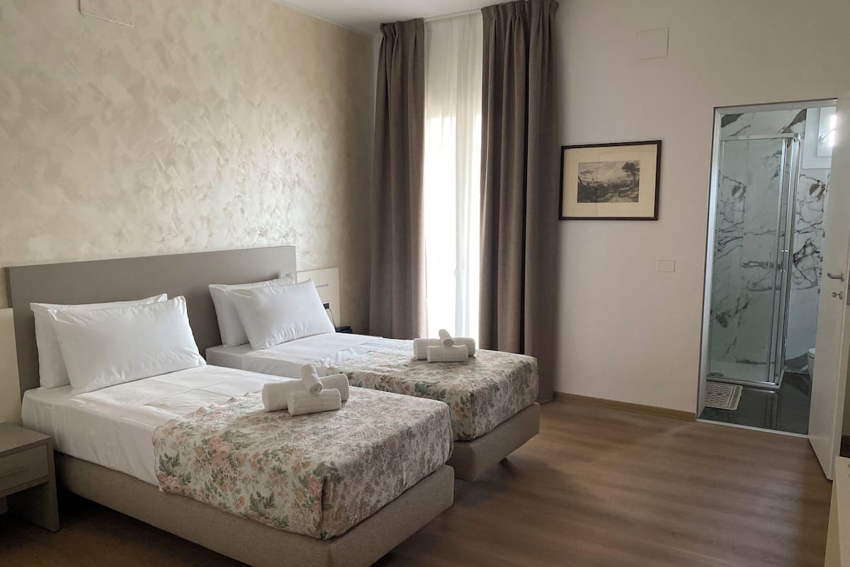 Quarto de hotel com duas camas, chuveiro e uma moldura na parede.