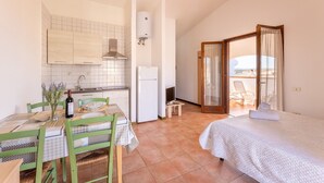A compact bedroom with a bed, a small kitchenette, and a balcony with a chair.