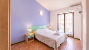 A bedroom with a bed, nightstand, and a window with curtains. - Casa Pavoncelle Apartments In Gallura - Casa Pineta (Santa Teresa Gallura)