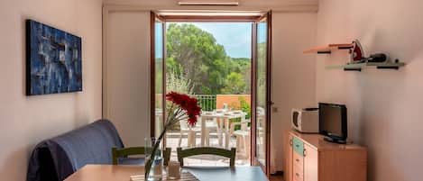 A compact kitchen with a dining area, a TV, and a view of greenery outside.