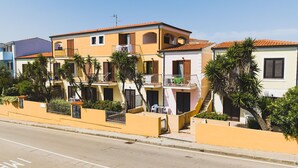 A row of Mediterranean-style buildings with balconies, a clear sky, and a road with parking spaces. - Casa Pavoncelle Apartments In Gallura - Casa Pineta (Santa Teresa Gallura)