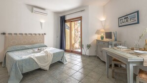A bedroom with a bed, a desk with a lamp, and a view of the outside. - Casa D'orso Green Village Sardegna (Palau)