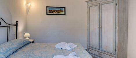 Un dormitorio con cama, mesita de noche, lámpara, armario y un cuadro en la pared.
