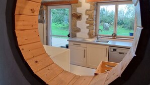 Rundblick durch ein Fenster auf eine Küche mit Holzbalken, Steinwänden und Blick ins Grüne.