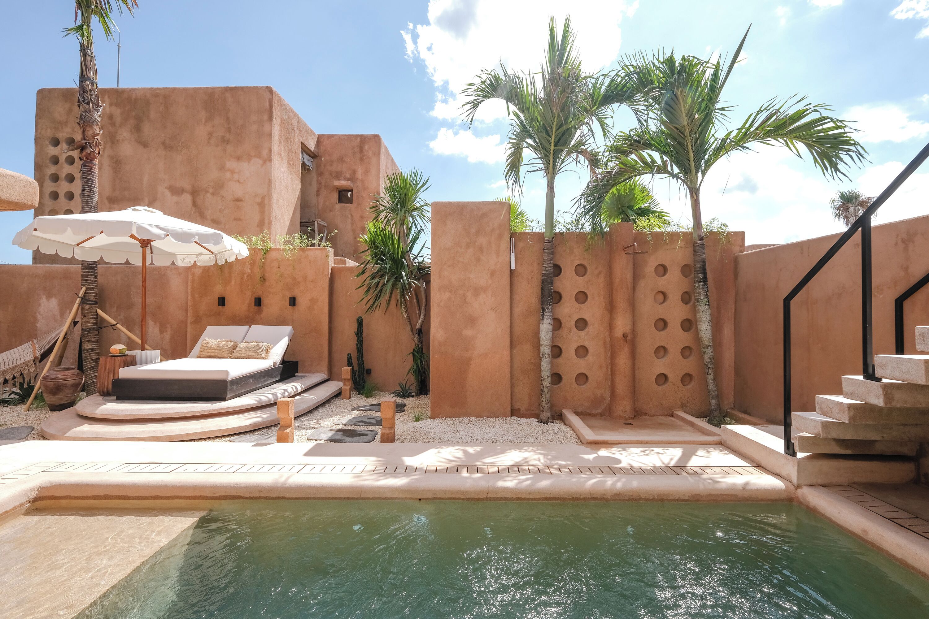 Zona de piscina con una tumbona, sombrilla y palmeras.