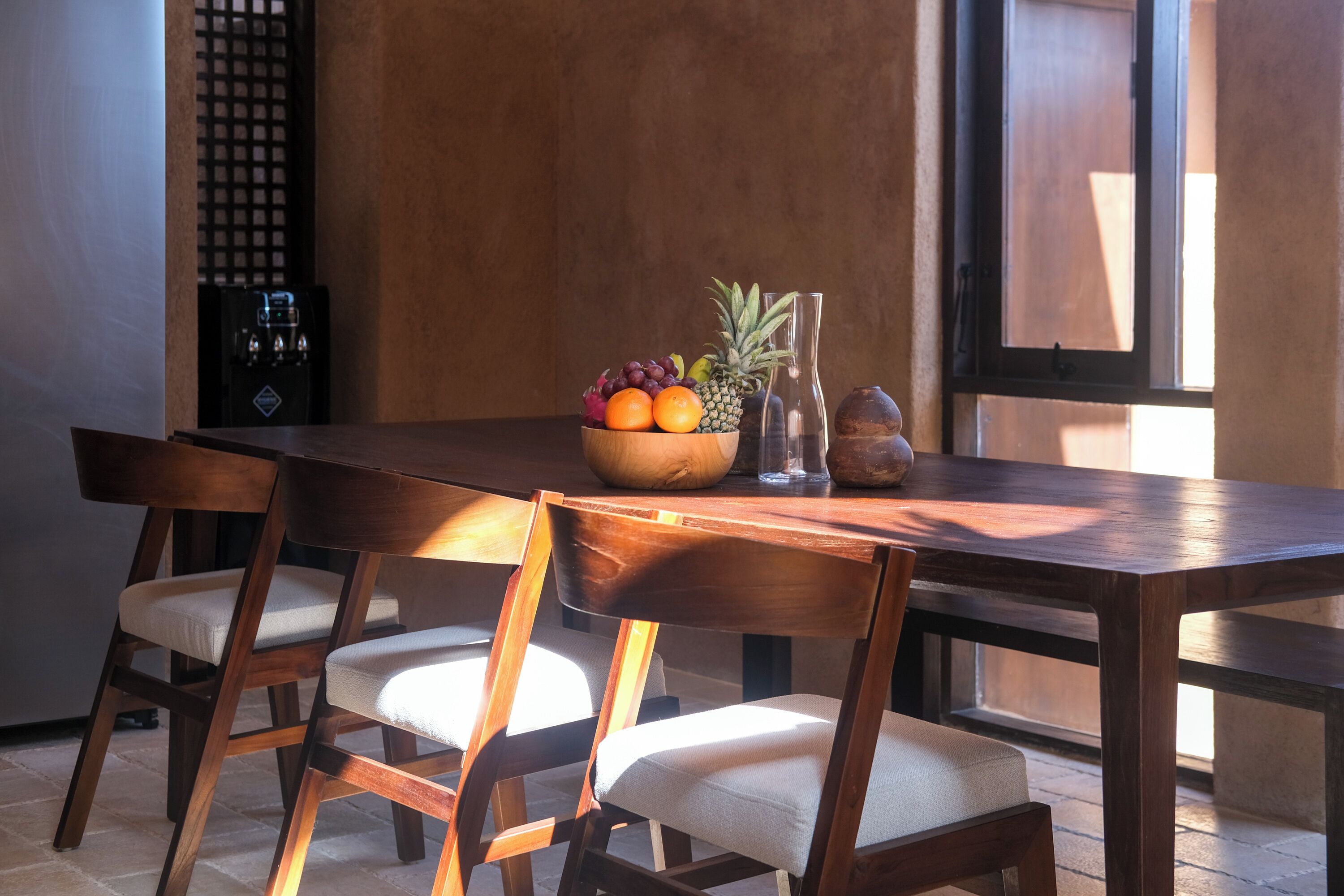 A wooden dining table with a fruit bowl, two chairs, and a coffee machine.