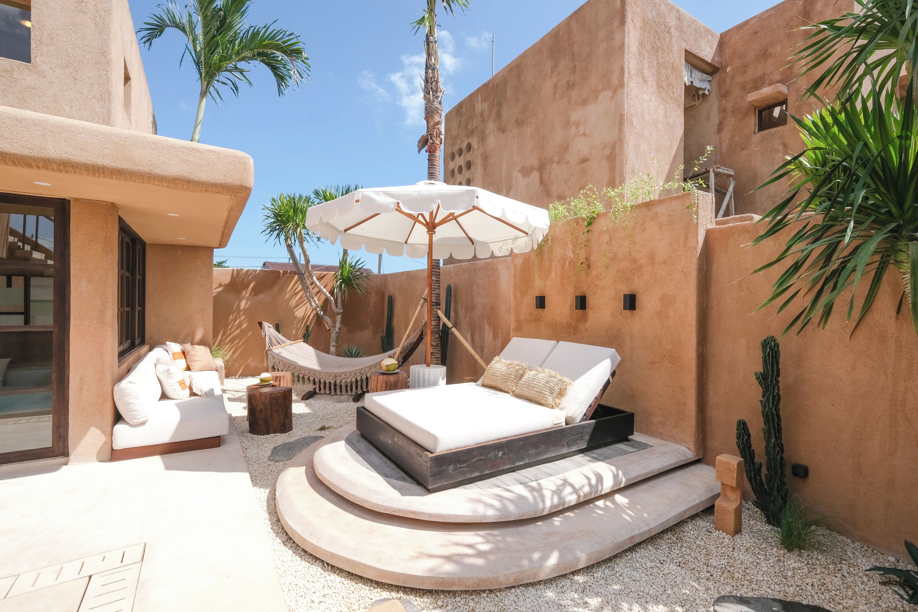 Un espacio exterior moderno con una cama, sillones de descanso y una hamaca.