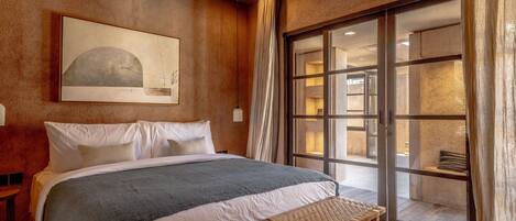 A bedroom with a large bed, a bench, a painting, and a view through a glass door.