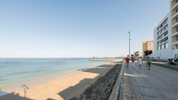 A coastal promenade with a sandy beach, a stone wall, and a modern building with balconies. - Velbar - Apartment In Cádiz. Free Wifi (, Cádiz)