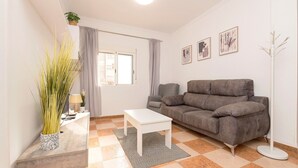 A living room with a sofa, a coffee table, a floor lamp, and a potted plant. - Velbar - Apartment In Cádiz. Free Wifi (, Cádiz)