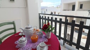 Een balkon met een ontbijttafel, inclusief een theepot, karaf, kopjes en een bloevas.
