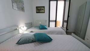 Een slaapkamer met twee bedden, elk met een blauwgroen kussen, een witte radiator en een kaart aan de muur.