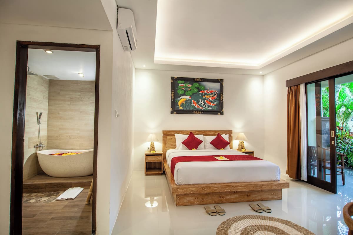 A modern hotel room with a large bed, a bathtub, and a view of greenery.
