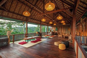 Una terraza de madera con asientos exteriores, techo con diseño y luces colgantes.